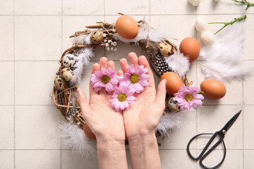 Woman making Easter wreath with eggs, feathers and flowers on white tile background