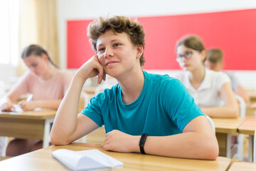 Teenager students sitting at desks and listening. Boy sitting in foreground and smiling.