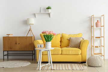 Interior of light living room with sofa and tulips in vase for International Women's Day