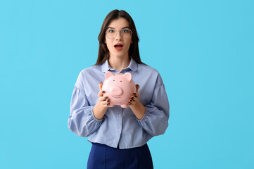 Beautiful young shocked woman with piggy bank on blue background