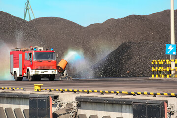 Fire truck spraying water on a black coal stockpile creating a rainbow