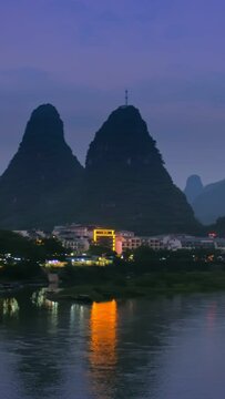 View of Yangshuo town illuminated in the evening with dramatic karst mountain landscape in background over Li river. Yangshuo, China. Horizontal camera pan