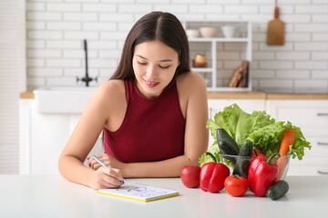 Obraz na płótnie Canvas Beautiful young Asian woman with fresh vegetables drawing nutrition diagram at home. Keto diet concept
