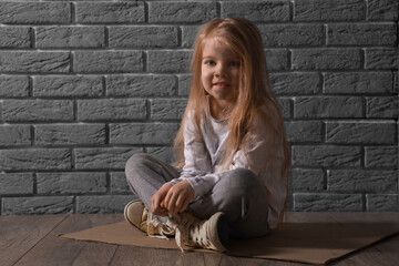 Homeless little girl sitting near grey brick wall