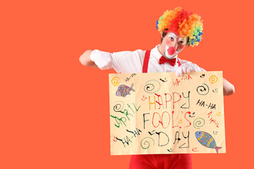 Portrait of clown pointing at poster with text HAPPY APRIL'S FOOL DAY on orange background