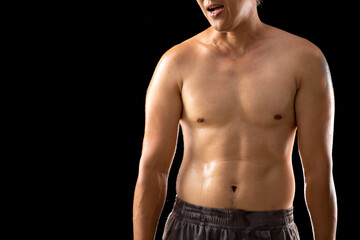 In a close-up shot against a black backdrop, the wet muscles of a young Asian man's body stand out,...