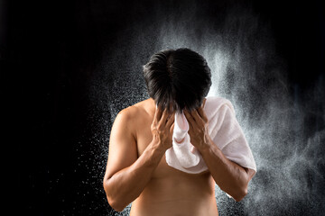 After a workout, an Asian young man dries his face with a white towel against a background of water...