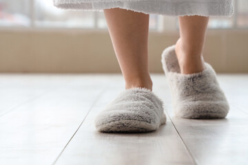 Woman in slippers walking on laminate floor at home, closeup