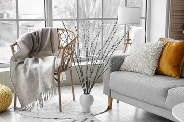 Vase with willow branches between armchair and sofa in living room