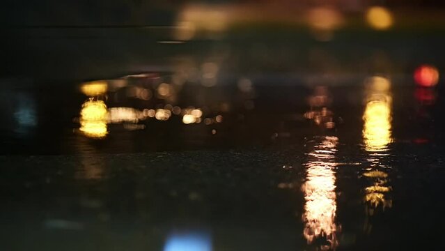 Atmospheric video of rainstorm in a night city.Heavy rain and splashes from cars passing through puddles taken from low point.Large drops break on the pavement in the light of street lamps.Slow motion