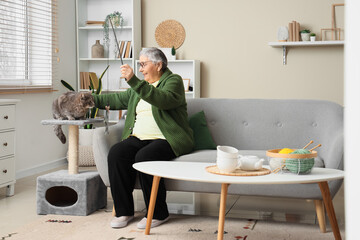Senior woman playing with cute cat on scratching post at home