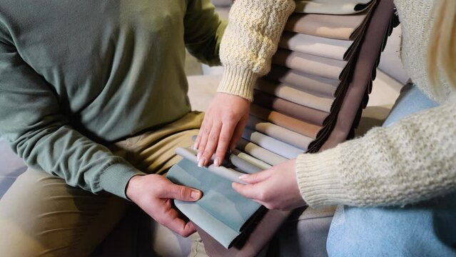 A man and woman choosing upholstery fabric color and texture from various colorful samples for sofa in a store, close up