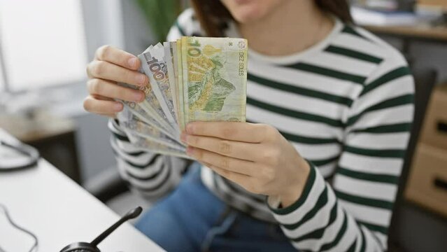 Young latina woman holding peruvian soles in a modern office, exuding financial confidence and success.