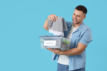 Young man holding box with charity clothes on blue background