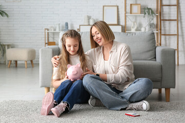 Mother and her daughter with piggy bank sitting on floor at home. Education savings concept