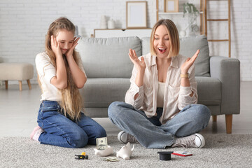Surprised mother and her daughter with broken piggy bank and money at home. Education savings...