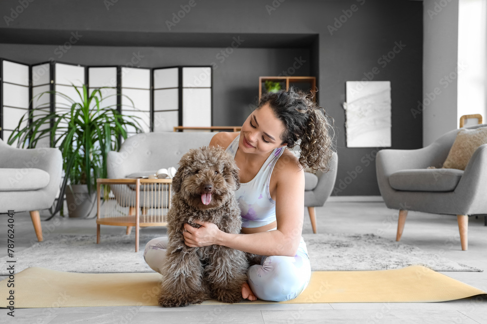 Sticker Sporty young woman with cute poodle sitting on mat at home