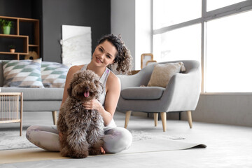 Sporty young woman with cute poodle sitting on mat at home