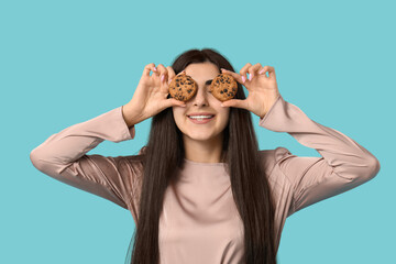 Beautiful young happy woman holding tasty cookies with chocolate chips on blue background