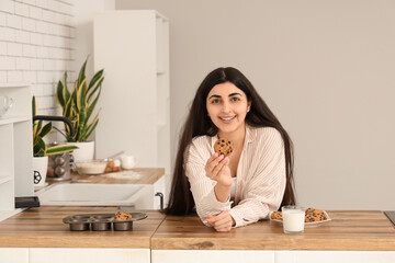 Beautiful young woman holding tasty cookies with chocolate chips and glass of milk at home