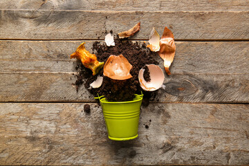 Bucket with organic waste and soil on wooden background. Compost recycling concept
