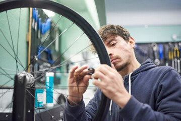 Hispanic man using a wrench tool to adjust the tension and tighten the spokes of a bicycle wheel in...