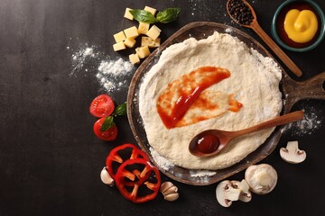 Pizza dough with tomato sauce and products on dark table, flat lay. Space for text