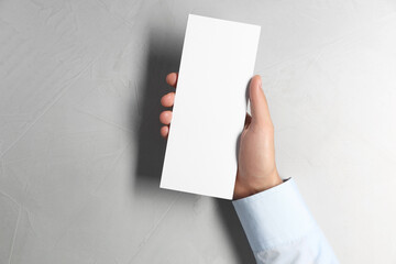 Man holding white blank card at light grey table, top view. Mockup for design