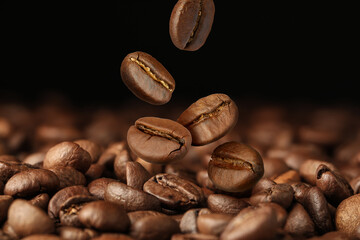 Roasted coffee beans falling on heap against dark background, closeup