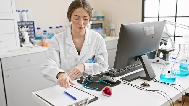 A woman scientist works in a laboratory with computer, microscope, and chemical flasks, analyzing samples and taking notes.