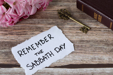 Remember the Sabbath Day, handwritten note with holy bible, ancient key, and spring flower on wooden table. Christian obedience, keeping the commandments, rest for the people of God, biblical concept.