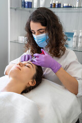 Cosmetologist making rejuvenating anti wrinkles injections on the forehead of a beautiful woman. Female aesthetic cosmetology in a beauty salon.