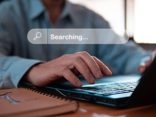 Close-up person typing or searching information via internet technology in laptops on wood table in room or office.
