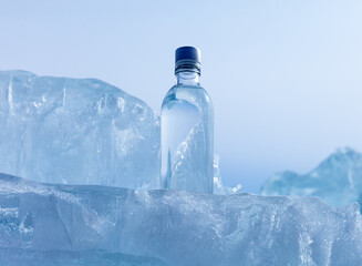 Glass bottle with cold natural drinking water stands on blue natural ice podium against background...