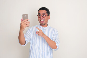 Adult Asian man looking and pointing to phone that he hold with wow face expression