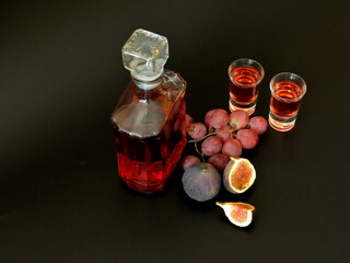 Grape-fig liqueur in two glasses and a bottle, as well as ripe fruit fruits on a black background.