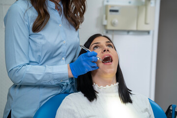 Young Caucasian dark hair woman with her mouth open having her teeth examined by the professional 