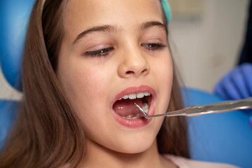 Closeup of cute little girl at dentist, open mouth , dentist looking her mouth with mirror tool 