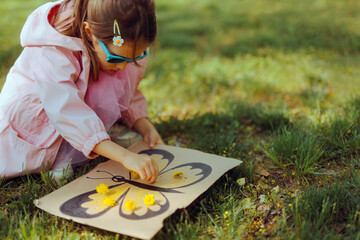 Kid with a DIY Cardboard Spring Activity with Flowers. Happy toddler girl making a handmade...