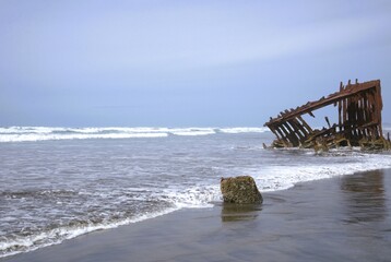 Metal frame of a ship washed up on the shore, a part of the Peter Iredale Shipwreck, with waves...