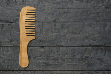 A classic wooden comb with a handle on a wooden background.