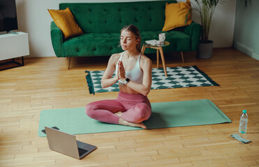 Young woman relaxing on a yoga mat in front of a laptop on a hardwood floor