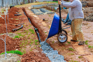 Crushed stone is fills into drainage pipes by worker using wheelbarrow