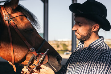 Man taking care of his brown horse in an equestrian center