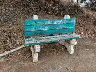 A green bench with a broken back sits on a rocky hillside