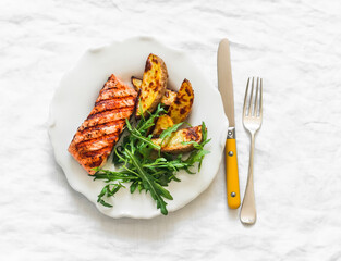 Delicious lunch - grilled salmon, baked potatoes and arugula salad on a light background, top view