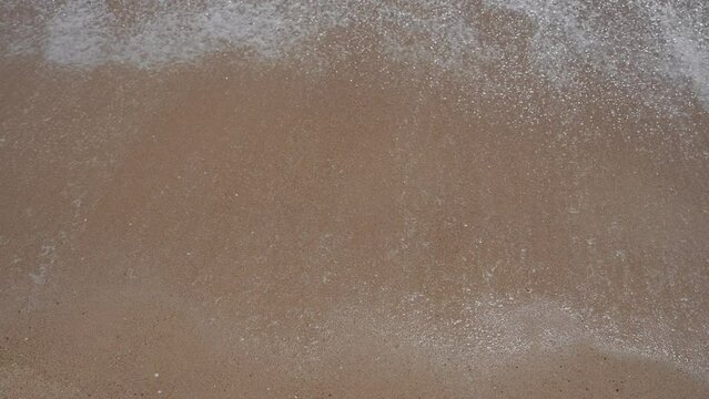 Foamy sea surf washes over golden sandy beach symbolizing tranquility and nature.