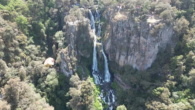 Toma a&eacute;rea de una cascada entre &aacute;rboles que cae de una monta&ntilde;a hasta el final en donde se convierte en un peque&ntilde;o r&iacute;o