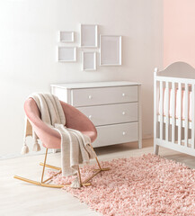 Delightful baby girl's nursery with a pristine white traditional crib, an elegant dusty pink upholstered rocking chair, and a luxurious blush shag rug, white photo frames on a pastel pink accent wall