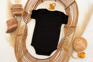 Black baby bodysuit lying in a rattan cot surrounded by baby toys and dummy